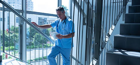 Male doctor walking up stairs in hospital reading tablet